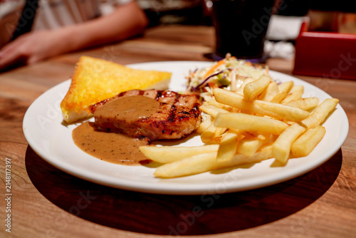 Canvastavla Grilled pork chop topped with savory brown gravy served with crispy golden French fries, buttered toast, and fresh coleslaw on a white plate