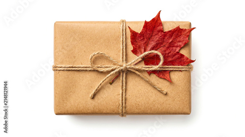 Gift box wrapped in brown paper with a red maple leaf isolated on white background
