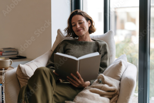 A woman deeply engrossed in a book, enjoying her quiet time on a plush couch, highlighted by soft light and a relaxed atmosphere that invites tranquility and contemplation.