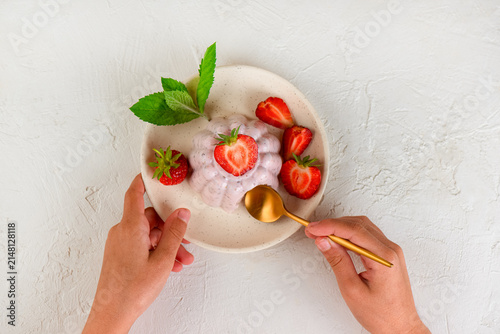Fresh strawberry chia jelly dessert with cottage cheese in a plate with the children's hands. Top view.