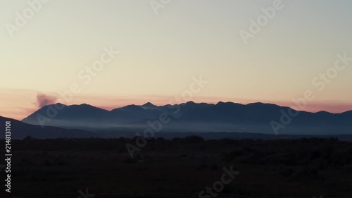 Wildfire smoke plume rising from mountain range at sunset