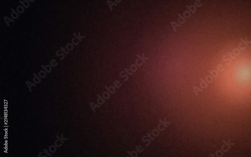A warm glowing orange light flare on the right side of a dark black background, creating a soft and atmospheric gradient with a hazy texture