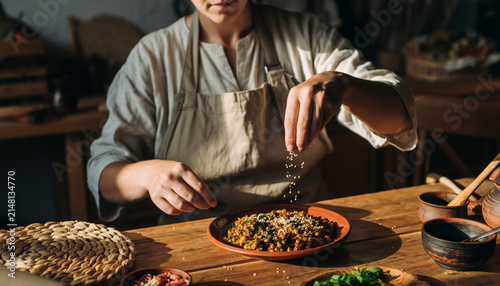 Person seasoning a plate of food in a cozy kitchen setting.
