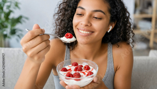 Young woman eating yogurt with fresh raspberries from a glass bowl