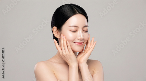 Young Asian woman with clear skin smiling and touching her face