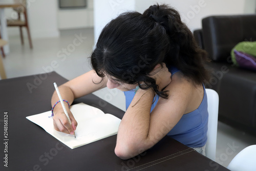Teenager writing in a notebook at the table at home