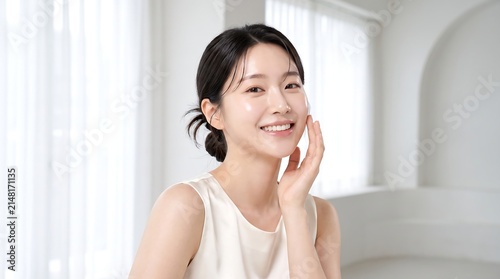Young Asian woman with glowing clear skin smiling for beauty skincare advertisement in bright minimalist room home.
