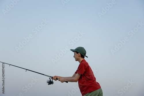 Teenager fish with rod under clear open sky