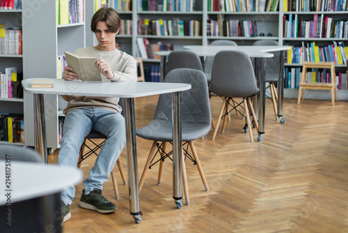 Obraz na płótnie Teenage boy immersed in literature in a vibrant school library setting