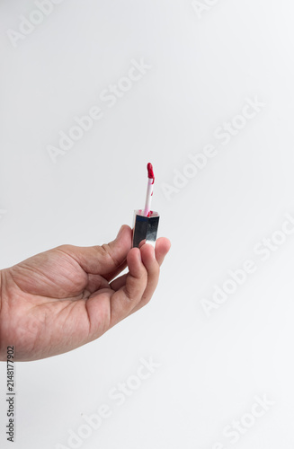 Hand holding red liquid lipstick tube and applicator wand isolated on white background