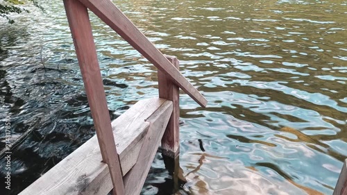 A rustic wooden ladder extends from a weathered dock into the clear, rippling waters of an alpine lake in Austria, surrounded by natural reflections and serene mountain nature.