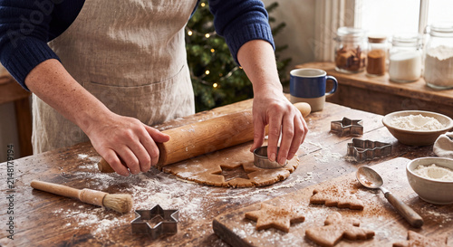 A person uses a rolling pin to flatten cookie dough on a rustic wooden kitchen table surrounded by baking ingredients.