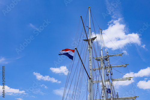 Obraz na plátně Dutch flag waving on the mast of a tall sailing ship against a bright blue sky w