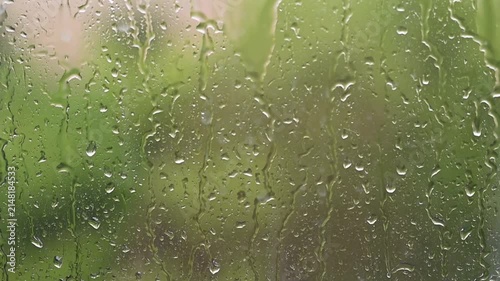 Raindrops falling down a window pane during a storm Heavy rain on glass surface with blurry green nature background