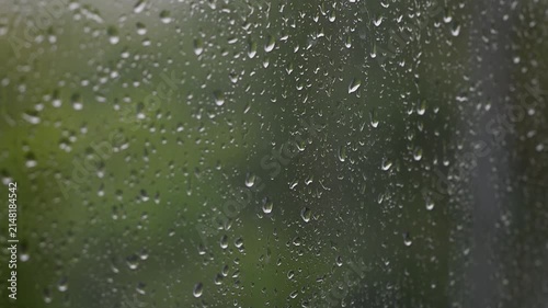 Raindrops falling down a window pane during a storm Heavy rain on glass surface with nature background blurry green