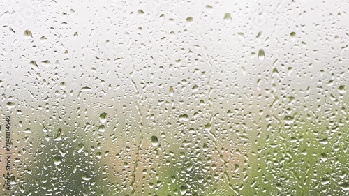 Raindrops falling down a window pane during a storm Heavy rain on glass surface with green nature background blurry