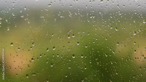 Raindrops falling down a window pane during a storm Heavy rain on glass surface with background blurry green nature