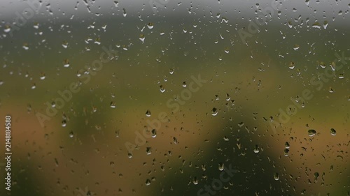 Raindrops falling down a window pane during a storm Heavy rain on glass surface with green blurry background nature