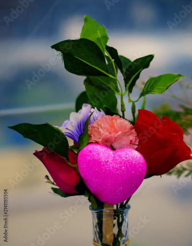 Colorful flowers in a vase with a heart shape decoration placed in a bright and lively indoor setting