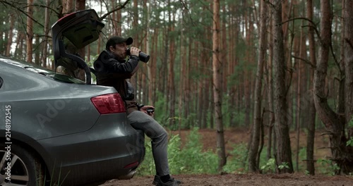 Male traveler resting in vehicle boot and drinking hot tea during road trip, audio included