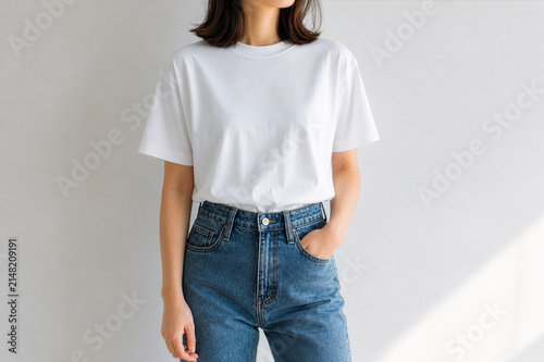 A young woman wearing a blank white t-shirt and blue denim jeans against a neutral background