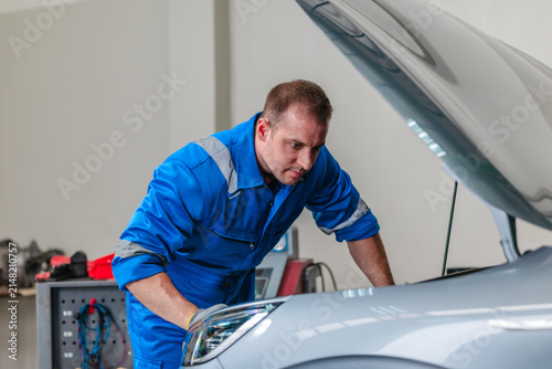 Mechanic using tester to check electric vehicle EV battery voltage under open hood in garage