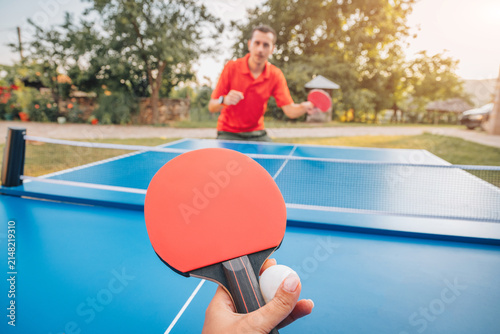 Foto POV first-person perspective of two players competing in an outdoor table tennis match on a sunny afternoon, opponent visible across the net