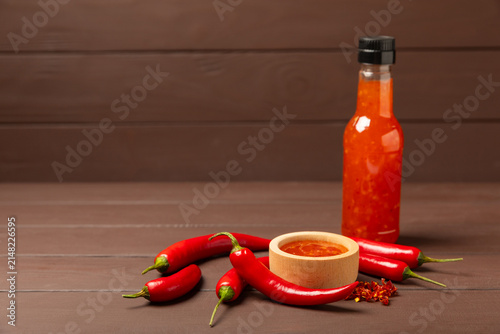 Obraz na płótnie Hot chili sauce  in a bowl with fresh red peppers and chili flakes on wooden cutting board