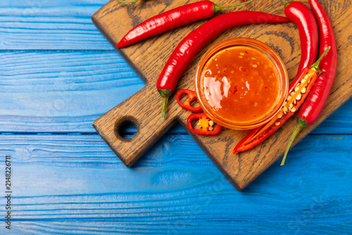Konstfotografi Hot chili sauce  in a bowl with fresh red peppers and chili flakes on wooden cutting board