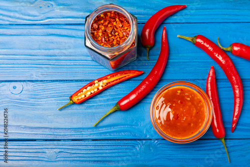 Obraz na płótnie Hot chili sauce  in a bowl with fresh red peppers and chili flakes on wooden cutting board
