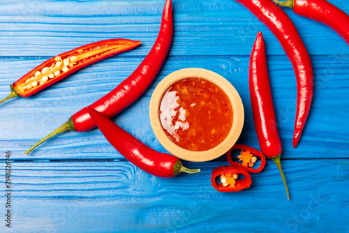 Fotografie Hot chili sauce  in a bowl with fresh red peppers and chili flakes on wooden cutting board