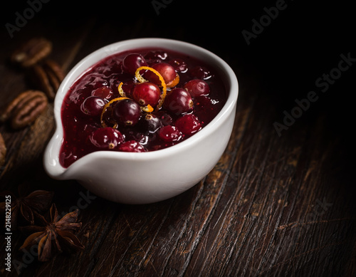 Vibrant homemade cranberry sauce with fresh orange zest in a white serving dish displayed on a dark rustic wooden table with pecans and star anise, perfect for holiday gatherings