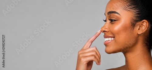 Retrato em perfil de uma linda mulher brasileira sorrindo e tocando a ponta do nariz. Conceito de beleza, cirurgia plástica, rinoplastia e cuidados com a pele. Fundo cinza com espaço para texto.