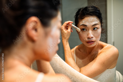 Woman applying facial mask with brush in bathroom mirror