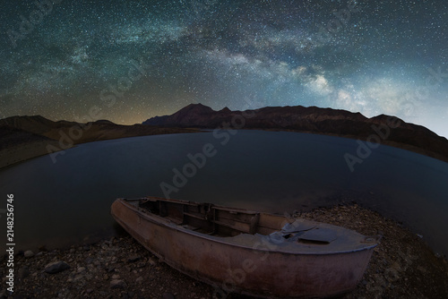 Old boat on the lake with mountains the against  Milky Way galaxy .Space, night landscape time lapse.