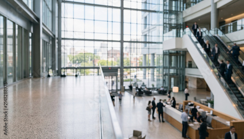 A spacious, modern lobby with large windows, showcasing a bright ambiance. Visitors engage while others use escalators in a busy urban building.