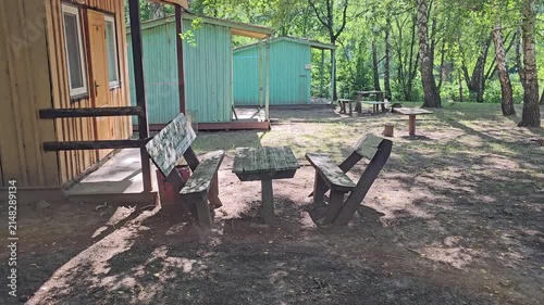 Small wooden cabins with picnic tables in a peaceful forest recreation area surrounded by tall trees on a sunny summer day