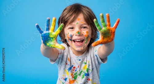 Smiling young child with colorful painted hands raised toward the camera against a bright blue background celebrating creativity, fun, and artistic expression.