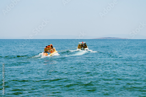 Speedboat towing a group of tourists on a fast inflatable banana boat ride on the sea waves close up.