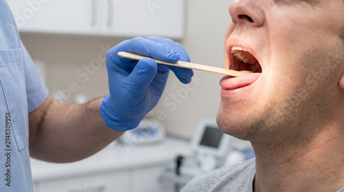 Doctor examining patient with tongue depressor in dental clinic