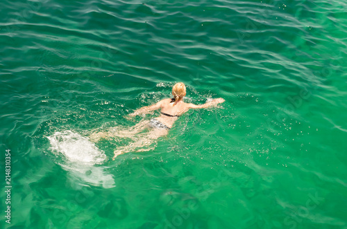 High angle view of a woman swimming in clear turquoise emerald sea water on a sunny summer day close up.