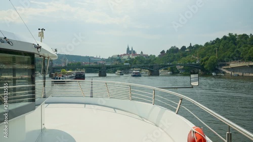 A tourist cruise boat sails along the Vltava River in Prague. Historic bridges and Prague Castle decorate the scenic urban skyline. Passengers enjoy sightseeing during a relaxing vacation.