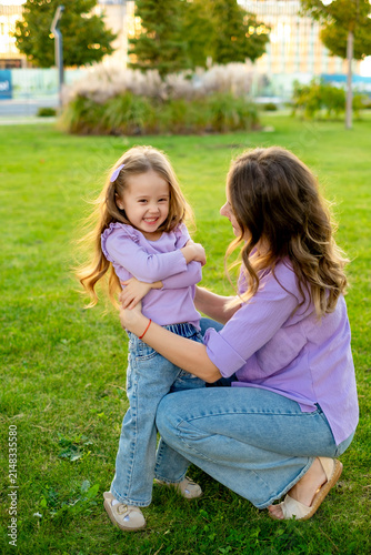 mother and child walking in the park in the summer, having fun together, mother and daughter hugging and kissing on a green lawn, motherly love