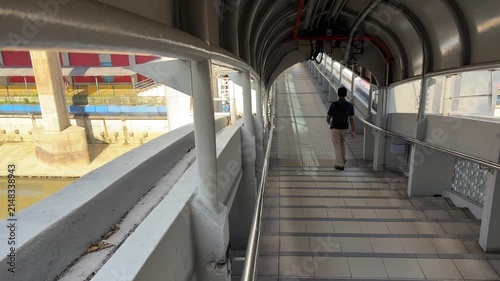 Daily commuters walking through modern pedestrian link bridge at KTM railway station in Kuala Lumpur city center.