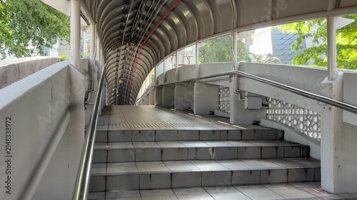 Daily commuters walking through modern pedestrian link bridge at KTM railway station in Kuala Lumpur city center.