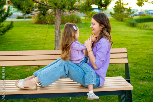 mother and child walking in the park in the summer, having fun together, mother and daughter hugging and kissing on a green lawn, motherly love