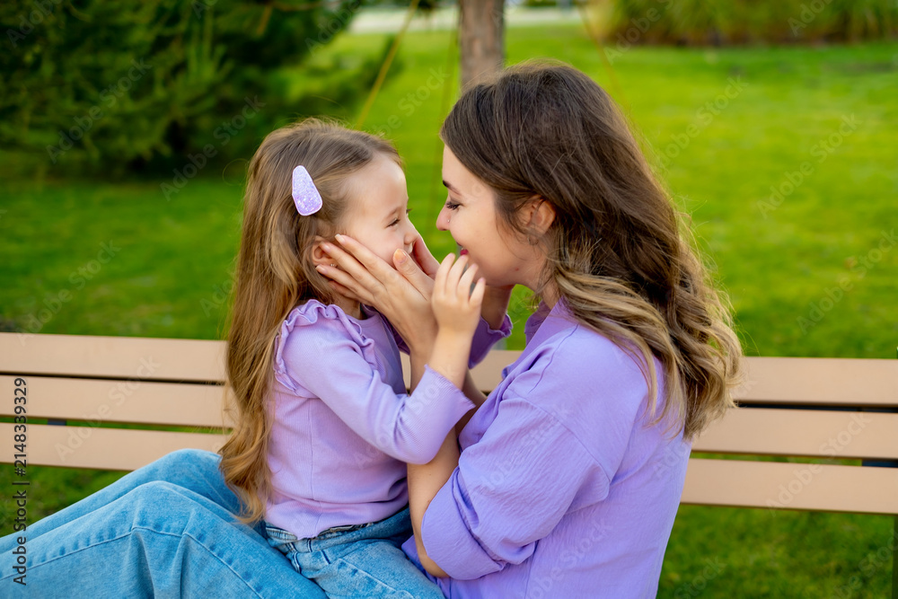 Fototapeta premium mother and child walking in the park in the summer, having fun together, mother and daughter hugging and kissing on a green lawn, motherly love