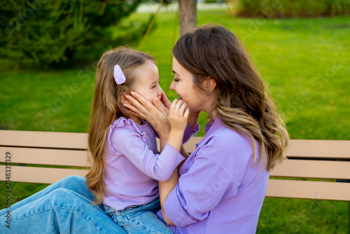 mother and child walking in the park in the summer, having fun together, mother and daughter hugging and kissing on a green lawn, motherly love