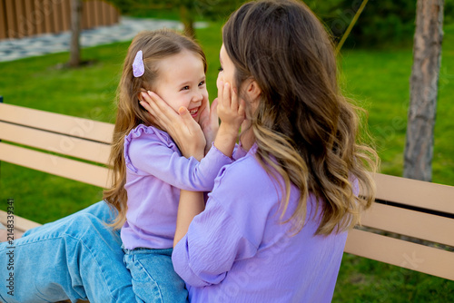 mother and child walking in the park in the summer, having fun together, mother and daughter hugging and kissing on a green lawn, motherly love