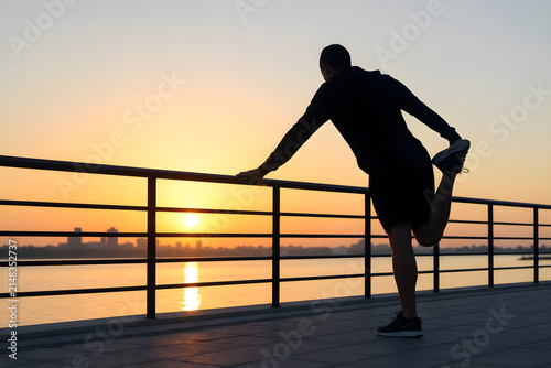 Runner stretching by waterfront railing at sunrise